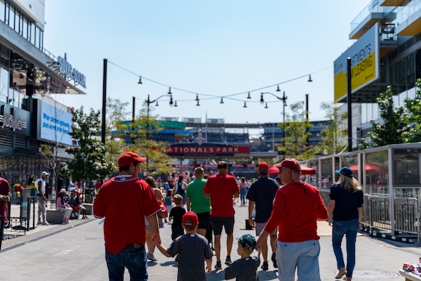 Fans in red jerseys walk toward Nationals Park in Washington, DC on a sunny day.