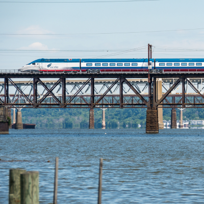 An Amtrak Acela train crosses a bridge over the Potomac River on a clear day.