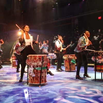 Performers in sequined jackets play festive drums on stage during a lively holiday show in Washington, DC.