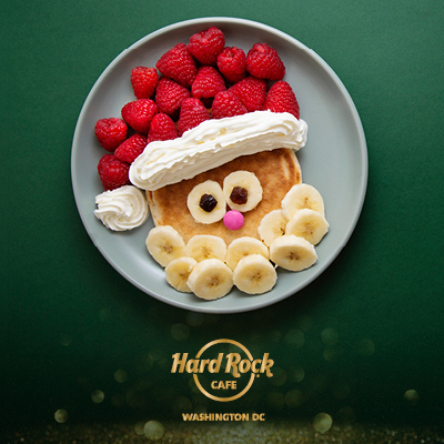 A pancake decorated with fruit and whipped cream to resemble Santa Claus sits on a plate with the Hard Rock Cafe Washington, DC logo below.