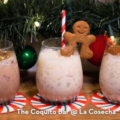 Three glasses lined up with festive touches like a peppermint straw and a gingerbread man, with a decorated tree in the background.