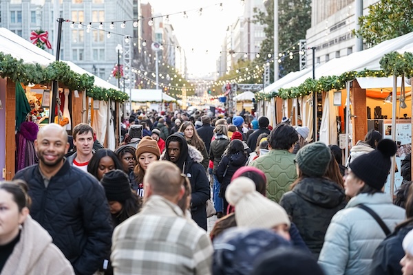 A large crowd explores vendor stalls decorated with greenery and lights at the Downtown Holiday Market in Washington, DC.