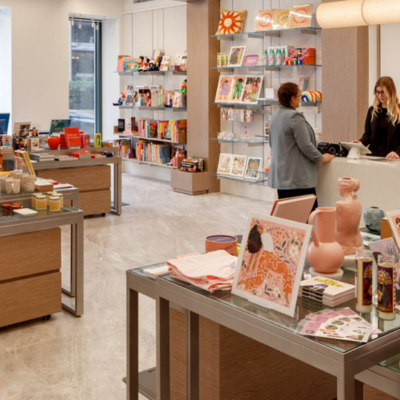 A modern museum gift shop in Washington, DC displays art books, stationery and curated gifts on neatly arranged tables as two people chat at the checkout counter.
