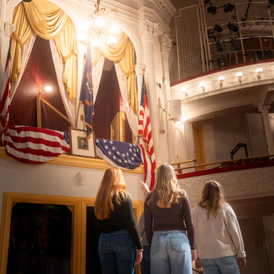 Three visitors look up at the historic presidential box draped in American flags inside Ford’s Theatre in Washington, DC.