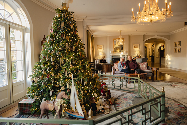 A large, decorated Christmas tree glows beside a couple relaxing in an elegant hotel lobby in Washington, DC.