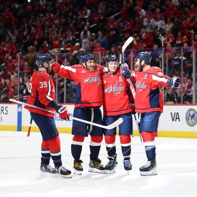 Washington Capitals players celebrate on the ice in front of a cheering crowd.