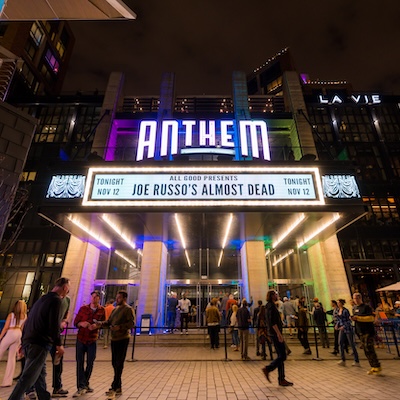 People gather outside The Anthem at The Wharf as its marquee glows with colorful lights.