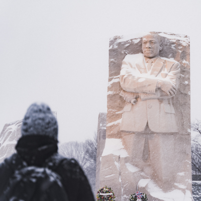A visitor looks toward a large stone memorial statue dusted with snow at the Martin Luther King, Jr. Memorial in Washington, DC.