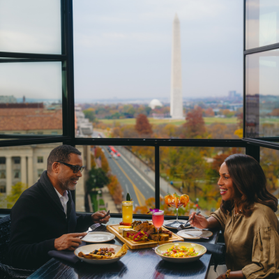 A couple enjoys colorful cocktails and dinner at a rooftop restaurant overlooking the Washington Monument in Washington, DC.