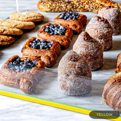 Assorted pastries including croissants, fruit danishes, and sugar-dusted rolls are neatly arranged in a bakery display case at Yellow in Washington, DC.