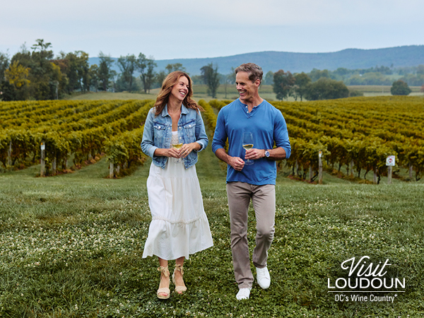 A couple sips white wine while strolling the lush grounds of Breaux Vineyards.