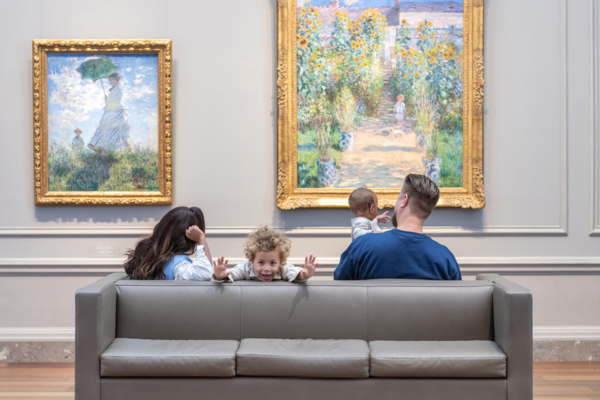 Family seated on a bench inside the National Gallery of Art, with two children and adults facing large Impressionist paintings in ornate gold frames.