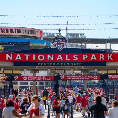 Crowds of fans entering Nationals Park through the center field gate on a sunny day, with stadium signage and Washington Nationals branding overhead.