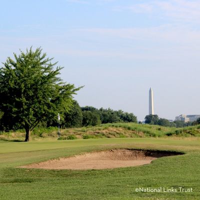 Golf course at East Potomac Park with a sand bunker and putting green in the foreground, and the Washington Monument visible in the distance beyond trees.