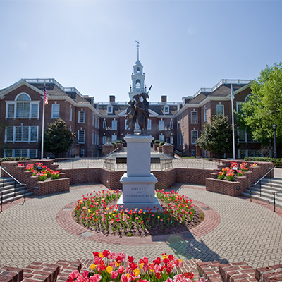 Exterior view of Legislative Hall, the state capitol building in Dover, Delaware, featuring the stately red-brick building framed by landscaped gardens and a central statue, symbolizing the state’s role in American governance and history.