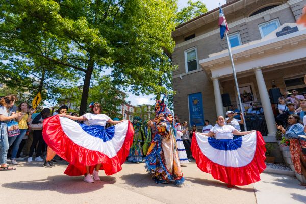 Performers dancing in traditional dress during Passport DC, with colorful skirts and costumes as a crowd gathers outside an embassy building.