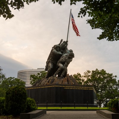 The Marine Corps War Memorial (Iwo Jima) with figures raising the American flag, set against trees and a cloudy sky.