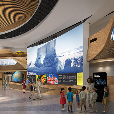 Visitors exploring the National Geographic Museum of Exploration, gathered in a modern gallery with a large immersive screen displaying icy landscapes and interactive exhibits throughout the space.