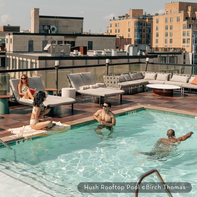 People relaxing and swimming at the Hush Rooftop Pool, surrounded by lounge seating and city views.