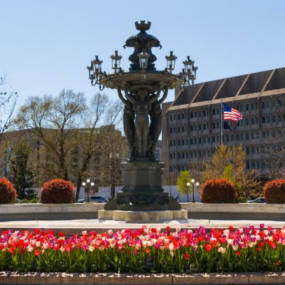 The Bartholdi Fountain at the U.S. Botanic Garden surrounded by blooming tulips and landscaped gardens on a sunny day.