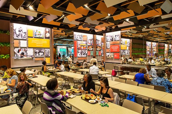 Visitors dining and gathering inside the Sweet Home Café at the National Museum of African American History and Culture, surrounded by colorful exhibit-style displays and large communal tables.