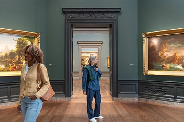 Visitors exploring a gallery at the National Gallery of Art, walking among framed landscape paintings displayed in a historic-style exhibition room.