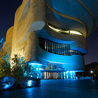 Exterior the entrance of the National Museum of the American Indian at night, illuminated by outdoor lighting.