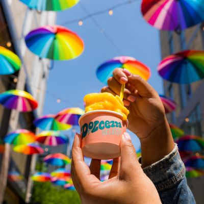 Hand holding a cup of gelato beneath colorful hanging umbrellas in Palmer Alley at CityCenterDC.