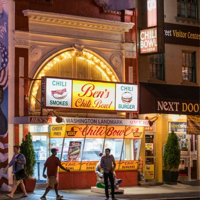 Ben’s Chili Bowl restaurant glowing at night along U Street, with its iconic neon signage and pedestrians passing by.