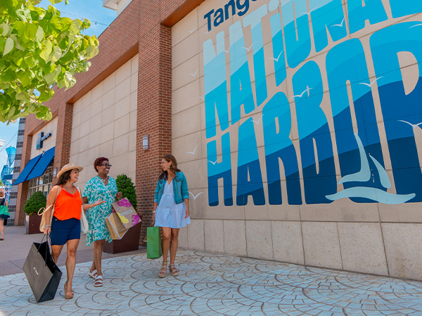 A group of three women talking and laughing while shopping at Tanger National Harbor.