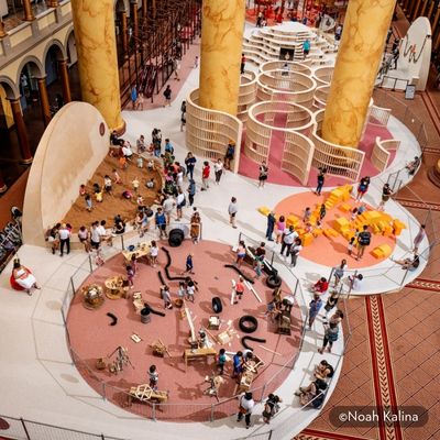 Overhead view of the National Building Museum’s PLAYGROUND exhibition, featuring hands-on building stations, a sand play area, foam blocks and a wooden maze.