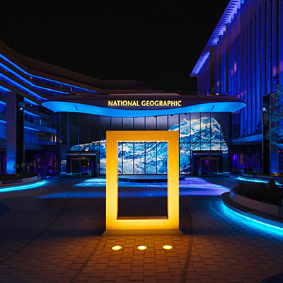 Illuminated National Geographic Museum entrance at night with the iconic yellow rectangle frame sculpture.