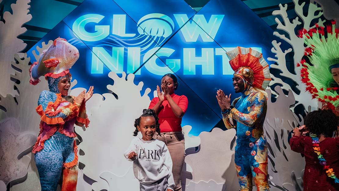 Families and guests enjoying Glow Nights at Georgia Aquarium with performers and signage