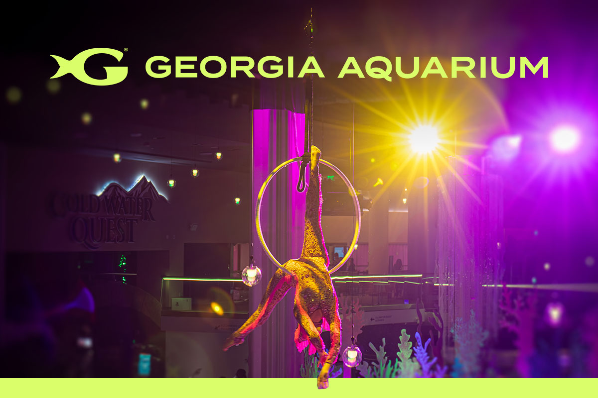 Performer in colorful costume with hula hoops under purple and pink lights at Georgia Aquarium's Glow Nights event, with "Where Wonder Glows" text overlay
