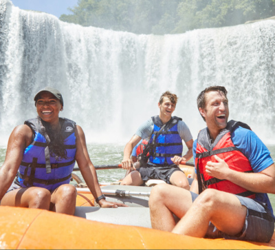 Two men and a woman smiling in a rafting boat at the base of Cumberland Falls