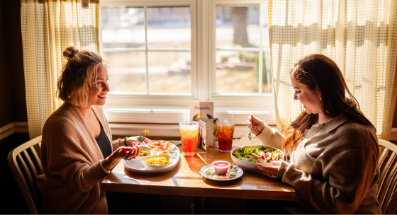 Two women at Back Home Restaurant in Elizabethtown, Kentucky, enjoying their meals and smiling at each other.