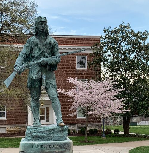Daniel Boone statue on EKU's campus with pink dogwood blooming in back