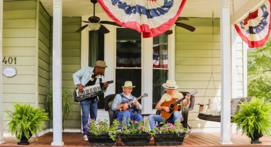 Musicians playing bluegrass instruments on a historic front porch