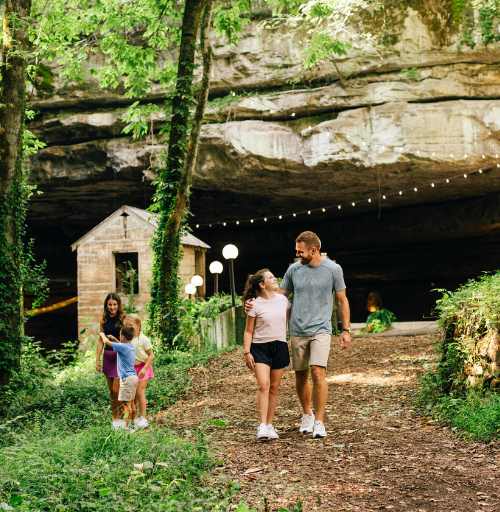 Family walking on hiking trails surrounding the entrance to a large cave opening.