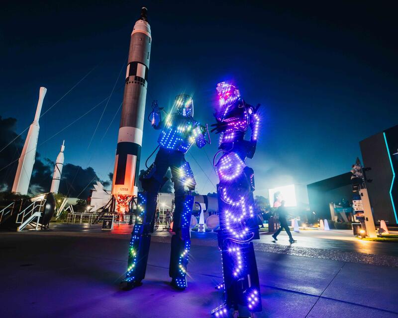 two people wearing lights standing next to a rocket
