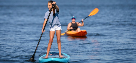 1 young girl paddleboarding and an adult kayaking behind