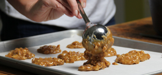 A pastry chef scoops pecan pralines onto parchment paper to cool.