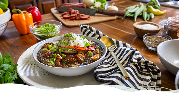 A bowl of gumbo sits atop a counter full of gumbo ingredients.
