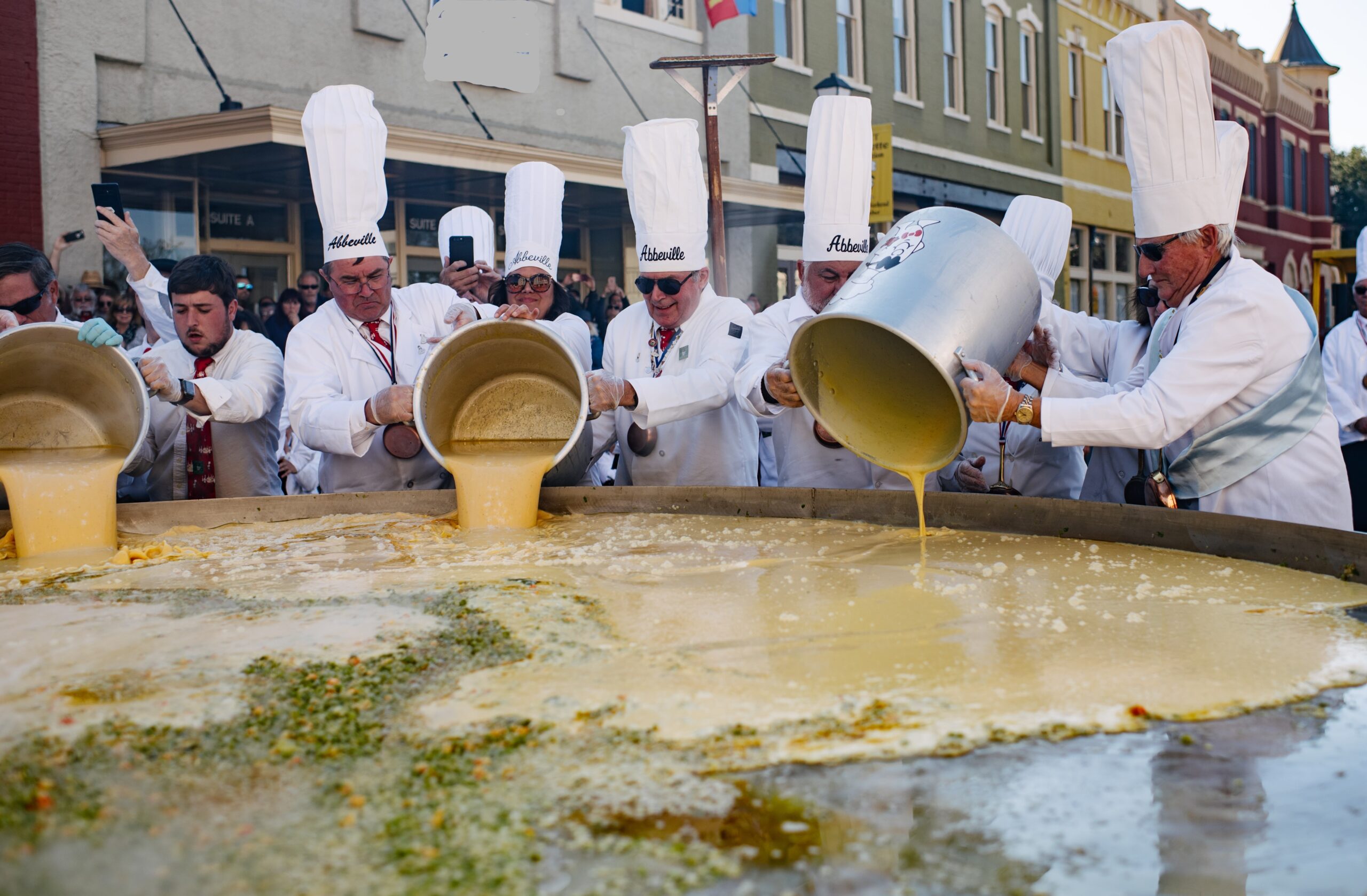 Chefs gathering around a giant skillet and pour eggs as they cook a giant omelette at Abbeville’s Giant Omelette Celebration.