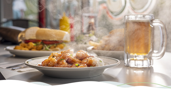 A steaming plate of shrimp étouffée placed beside a cold mug of beer and a shrimp po'boy. 