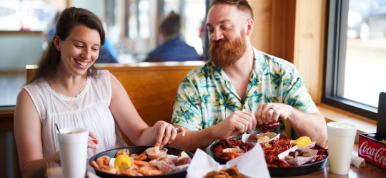 A man and woman eating a plate of boiled seafood. 