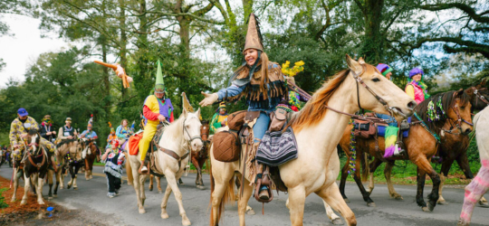A woman in costume riding a horse tosses a stuffed animal to a parade-goer.