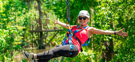 A person smiles from a zipline, where they are suspended.