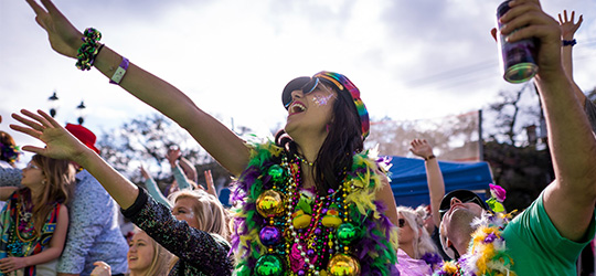 A woman dressed in purple, green and gold holds out an arm during a Mardi Gras parade.