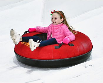 A child slides down a snowy hill on a red inner tube.